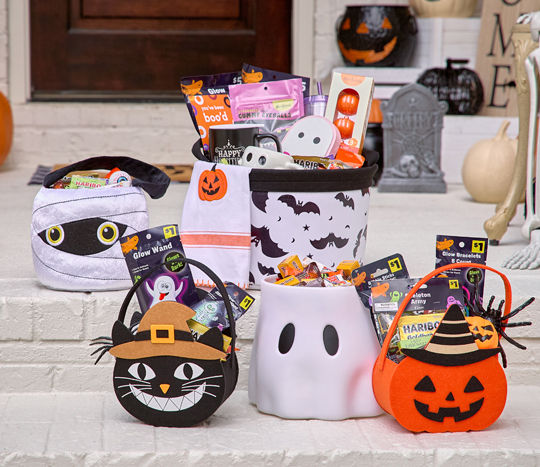 Halloween trick-or-treat buckets and bags filled with candy and goodies on a front porch decorated for Halloween. 