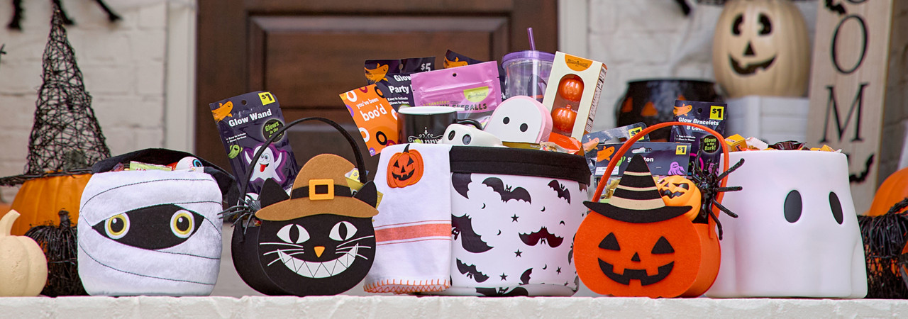 Halloween trick-or-treat buckets and bags filled with candy and goodies on a front porch decorated for Halloween. 