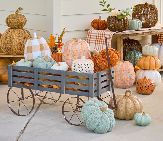 Fall pumpkins from pOpshelf in various materials, sizes, and colors piled in and around a rustic gray wagon.
