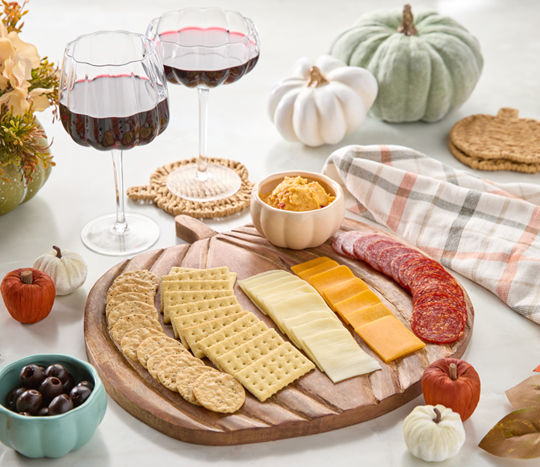 Wooden pumpkin-shaped charcuterie board, pumpkin wine glasses & coasters, with pumpkins and other, fall decor.