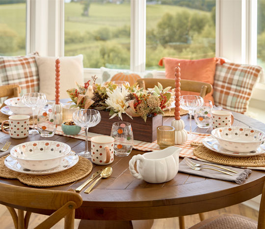 Table set with frall melamie pumpkin dinnerware, glassware, pumpkin-shaped wine glasses, and a stunning floral centerpiece.