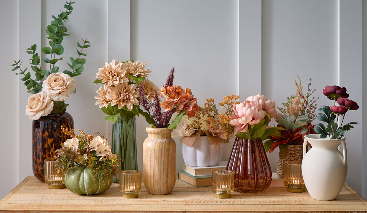 Fall floral bushes, branches, and picks in vases and premade fall floral arrangements on an entryway table.
