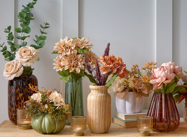 Fall floral bushes, branches, and picks in vases and premade fall floral arrangements on an entryway table.