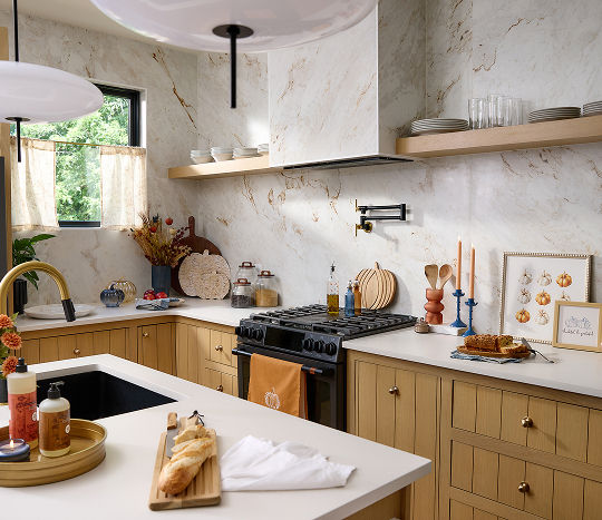 A neutral kitchen with wooden accents and marble wallpaper is decorated with fall themed decor featuring pumpkins and warm-toned autumn accents.