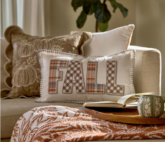Seasonal fall pillows from pOpshelf in shades of neutrals with plaid and pumpkin prints are displayed on a cream couch.