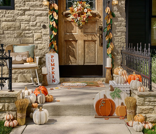 A front porch is decorated with fall themed outdoor decor from pOpshelf, including pumpkin-themed accents.
