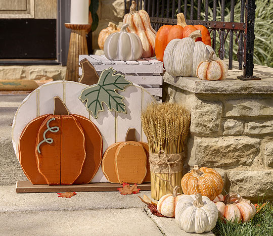 Faux pumpkins are displayed alongside a wooden pumpkin cutout on an outdoor porch staircase.