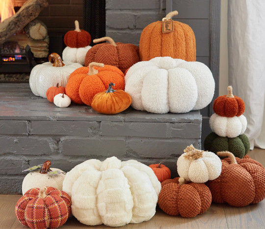 Fall pumpkins from pOpshelf in various materials, sizes, and colors piled on a gray brick fireplace hearth.