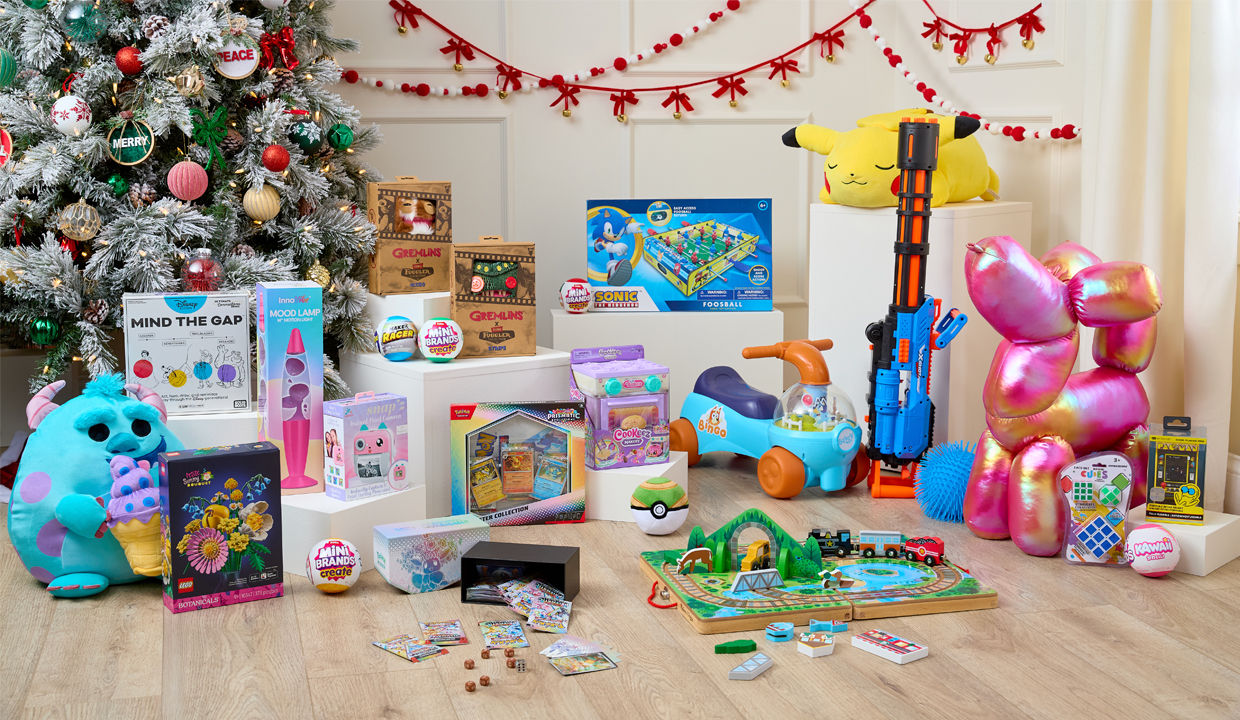 Toys in front of Christmas tree: Sonic air foosball table, pokemon plus, Melissa & Doug train set, giant balloon dog plush, Bluey ride-on, Fugglers, Mini Brands & more.