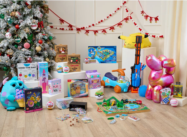 Toys in front of Christmas tree: Sonic air foosball table, pokemon plus, Melissa & Doug train set, giant balloon dog plush, Bluey ride-on, Fugglers, Mini Brands & more.