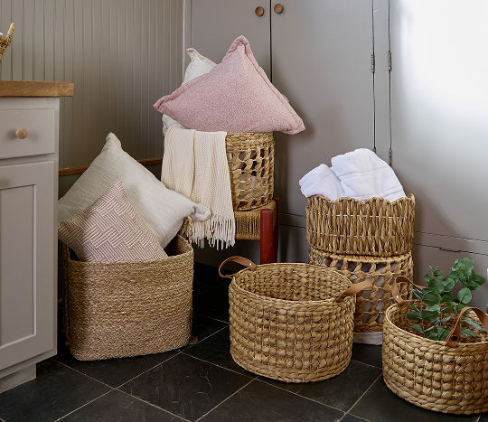 A living room corner displays wicker baskets from pOpshelf in various shapes and filled with soft plush blankets as well as luxuriously cozy throw blankets. 