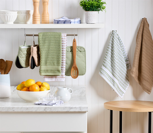 White kitchen with green, tan, and white kitchen towels, pot holders, and mini oven mitts.