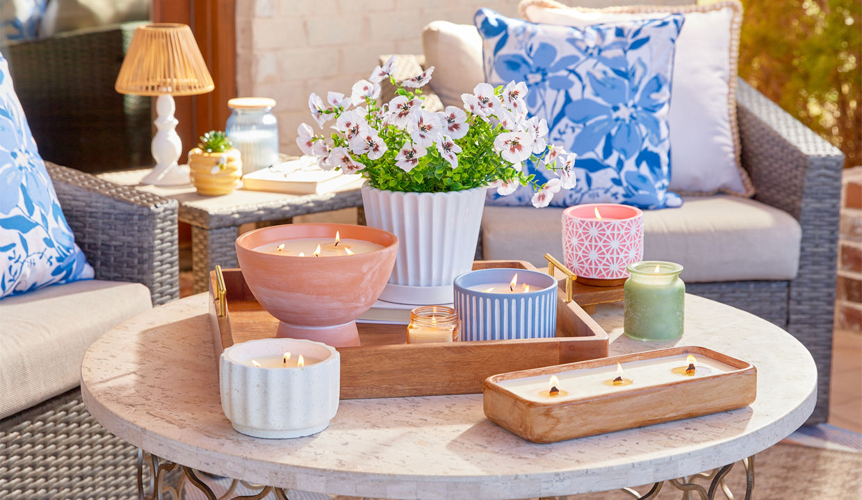 Various citronella candles in different colors, shapes and sizes on patio table
