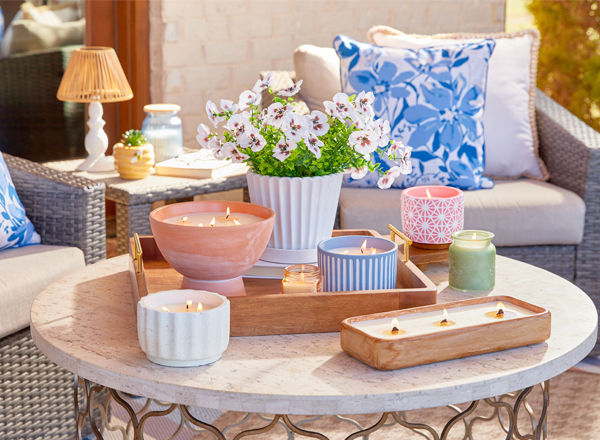 Various citronella candles in different colors, shapes and sizes on patio table