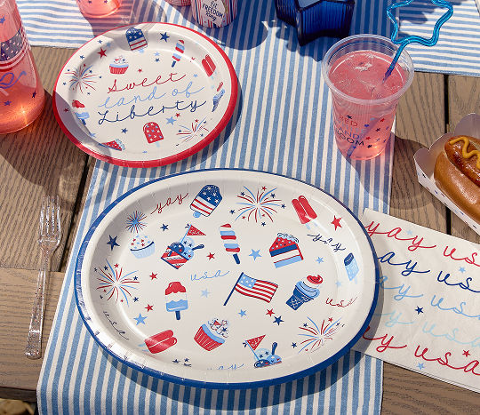 Patriotic paper plates are set on an outdoor dining table decorated with patriotic decor for the 4th of July.