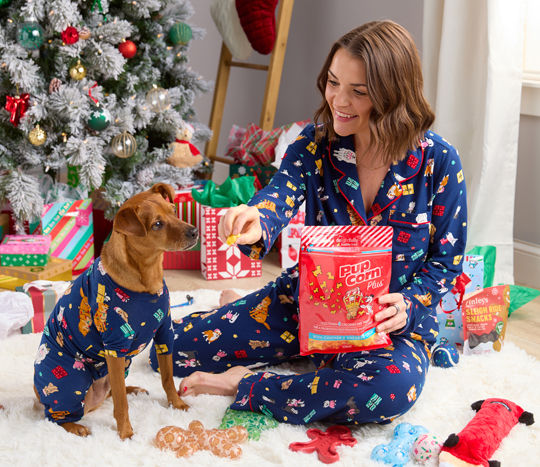 Girl and dog in front of Christmas Tree in matching PJs with pet toys and treats.