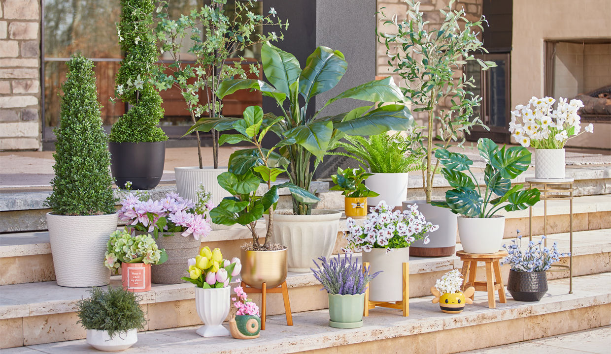 Various colors and designs of pOpshelf outdoor planters, flower pots, and plant stands filled with greenery and flowers on a patio.
