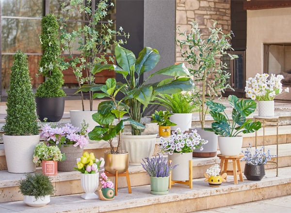Various colors and designs of pOpshelf outdoor planters, flower pots, and plant stands filled with greenery and flowers on a patio.