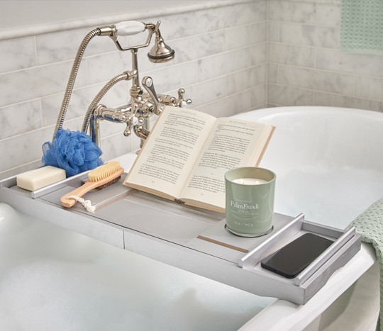 Bath caddy on tub with candle, scrub sponge, foot brush, candle & book.