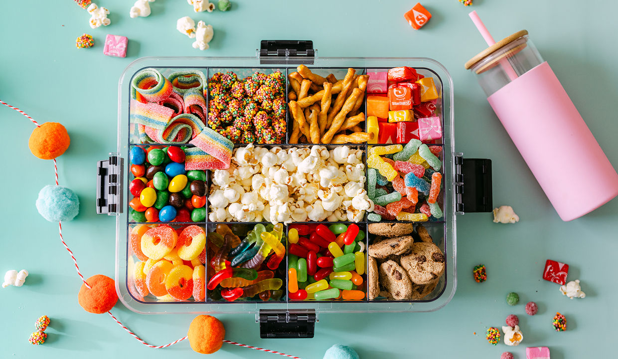 A snackle box from pOpshelf is filled with various snacks including gummy treats, popcorn, pretzels, and more with a water bottle featured lying beside the box.