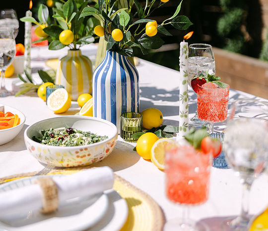 An outdoor table set for a summer backyard dinner party with colorful serveware and coastal Italian themed decor.