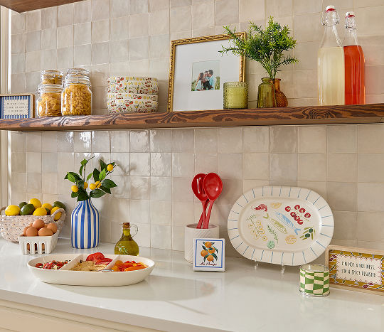A neutral kitchen countertop decorated with vibrant decorations and serveware featuring colorful coastal Italian inspired designs.