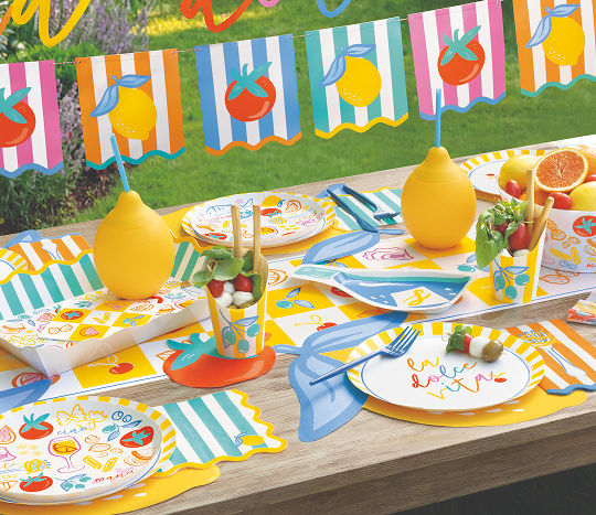A colorful backyard table is set with vibrant serveware featuring lemons, stripes, and food-themed inspired by coastal Italy.