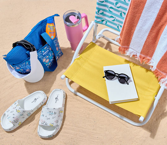 Beach chair, cooler bag, sunglasses, slides, and towel at the beach.