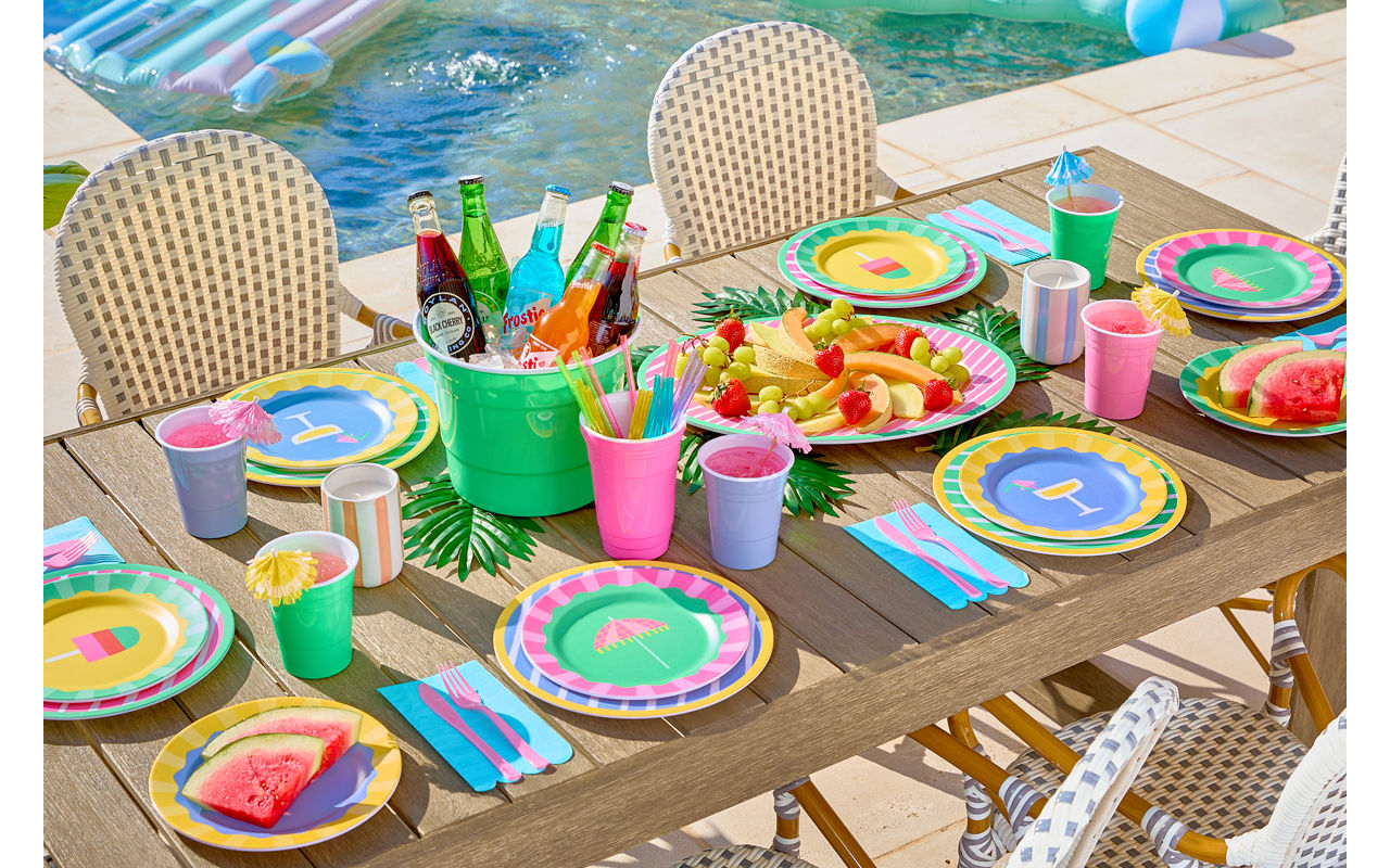 Poolside table set with colorful melamine dinnerware with stripes and summer icons, ice bucket, and matching drinkware.
