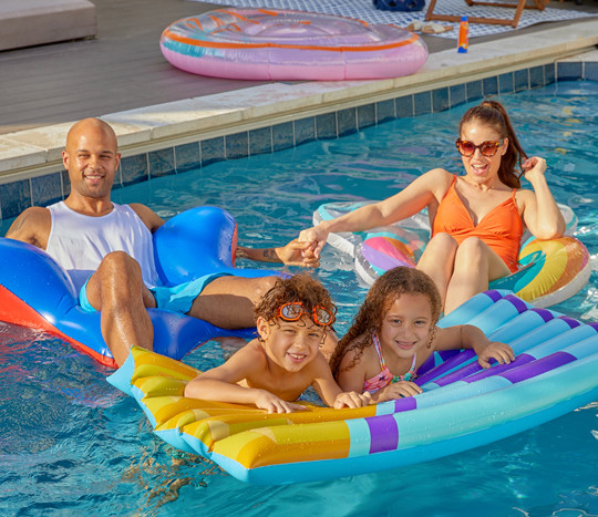 Mom, dad, and two kids in a swimming pool on color inflatable floats, swim rings, and rafts from pOpshelf.