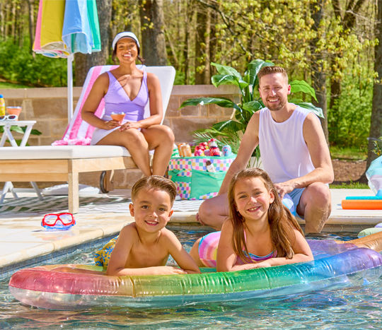 Family lounging and playing in the pool with towels, cooler, pool floats, goggles & more from pOpshelf.Lounge chairs with towels, pillows, white side table, rainbow umbrella, cooler, tote bags & accessories.