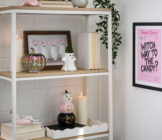 Shelving decorated with summer Halloween themed decorations featuring ghosts, pumpkin accents, and witch hats in a pink, black, and white color palette.