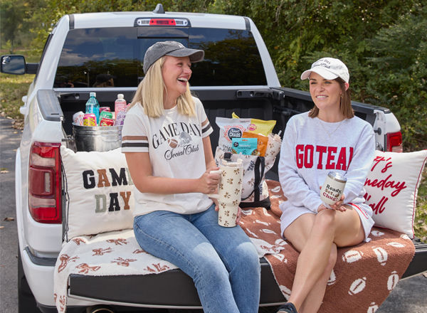Girls at tailgating party with football-themed blankets, pillows, travel cups & apparel, and tailgating snacks.