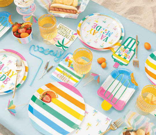 An outdoor dining table set with colorful vacation themed party supplies featuring tropical palm trees and popsicle shaped plates.