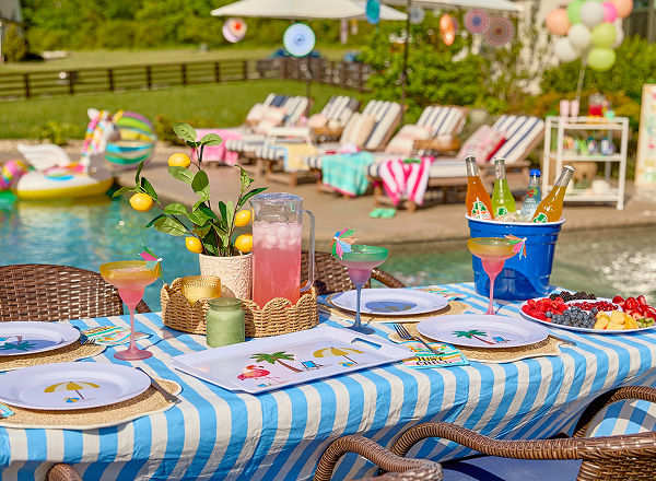 A poolside dining table decorated with colorful tropical decor, serveware, and dishware from pOpshelf.