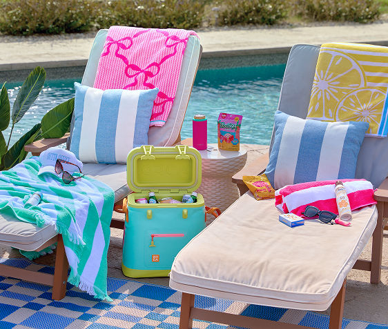 Two lounge chairs sitting poolside with towels, sunglasses, sunscreen and other pool day essentials on them.