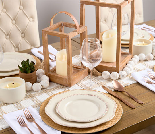 Table set with cream colored dinnereware accented with wood lanterns and copper flatware.