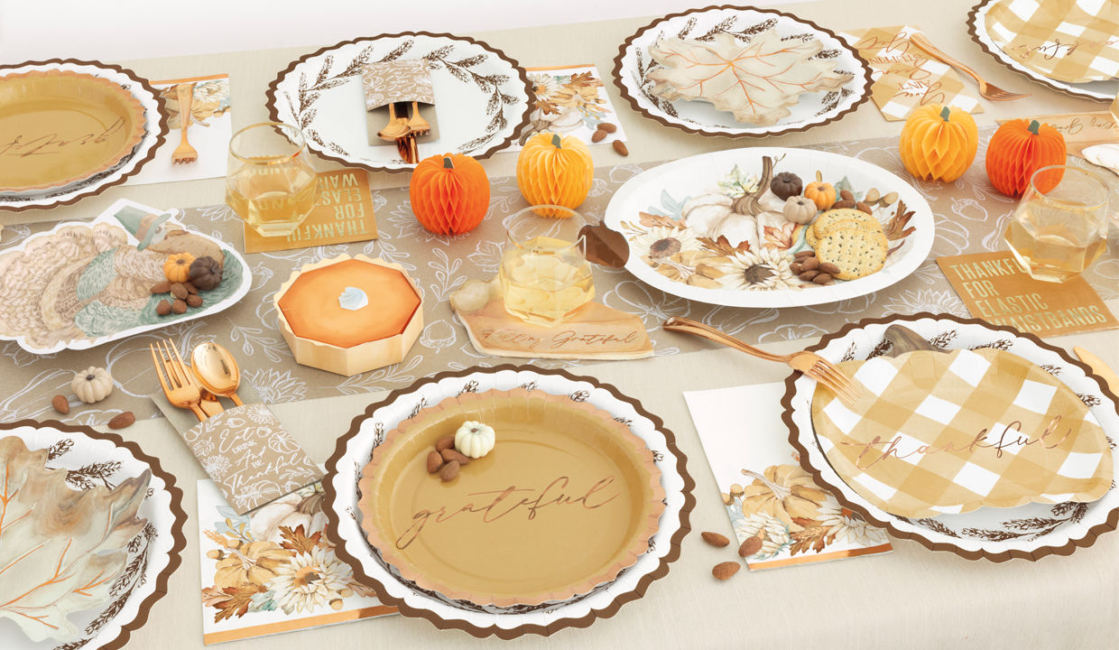 Fall party table set with pumpkin, turkey, and leaf shaped plates, round harvest plates, napkins, gold party utensils, and fall & pumpkin table decor.