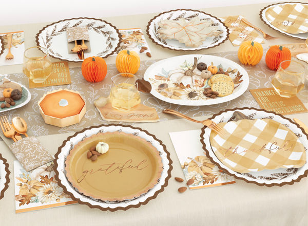 Fall party table set with pumpkin, turkey, and leaf shaped plates, round harvest plates, napkins, gold party utensils, and fall & pumpkin table decor.