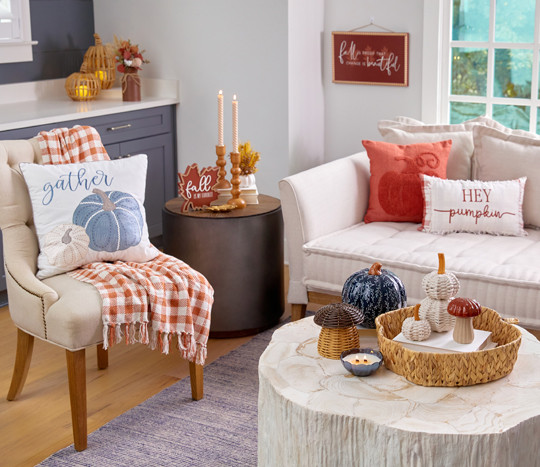 Den decorated for fall with blue pumpkin pillow, throw, wicker and metal pumpkin decor, fall wooden candleholders, and fall floral.