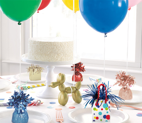 Party table decorated with several designs of balloon weight weighing down party balloons.