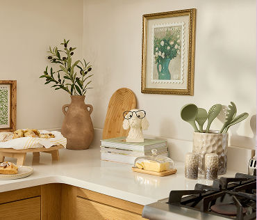 Kitchen counter with butter dish, vase, flowers, books, artwork, dog decor, tray with pastries.
