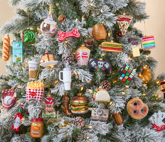 Glass novelty ornaments in a variety of designs on a flocked tree: popcorn, pretzel, taco, lipstick, polaroid camera, baseball & glove, rubik's cube & more.