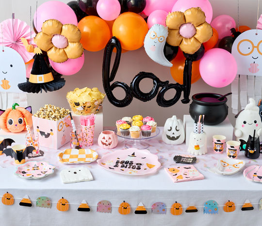 Halloween party table set with party supplies in pastel colors with black accents, a 'boo' balloon, bat streamers, haunted house cupcake stand, ghost plates, and more.