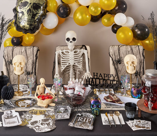 Creepy skeleton-themed Halloween party table set with skulls, coffin- and poison-bottle-shaped plates, spider webbing & more.