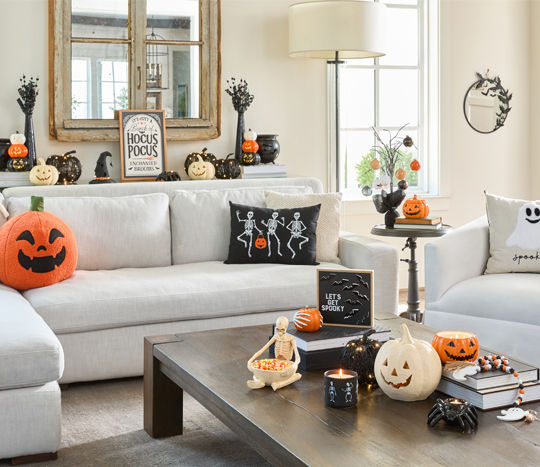 Living room decorated for Halloween with Jack-O-Lanterns in various designs, ghost and skeleton pillows, witch hat and cauldron, skeleton bowl, bat mirror, spider candleholder & more.