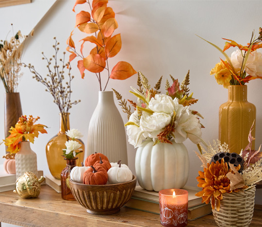 Fall floral bushes, branches, and picks in vases and premade fall floral arrangements on an entryway table.