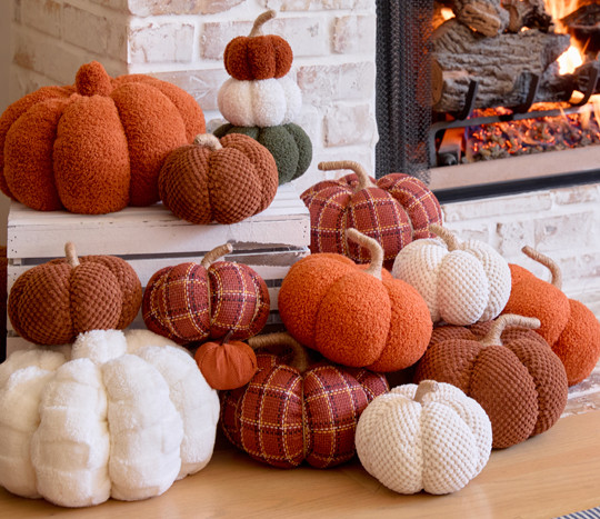 Fall pumpkins from pOpshelf in various materials, sizes, and colors piled on a gray brick fireplace hearth.