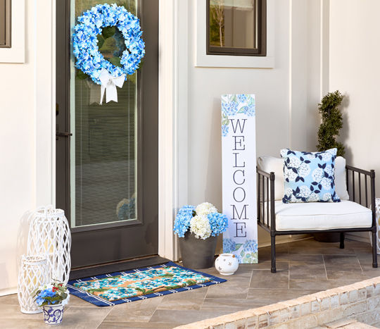 Front porch decorated with blue hydrangea Americana decor: wreath, pillow, porch leaner, doormat & more.