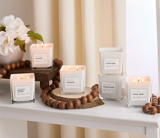 lit square candles with curtain background surrounded by white flowers and wooden beaded garland